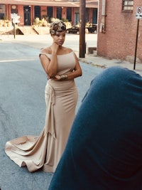 a woman in a beige dress is standing in front of a camera