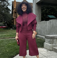 a woman in a burgundy suit standing on a sidewalk