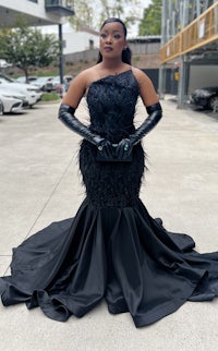 a woman in a black gown and gloves posing in a parking lot