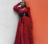 a woman in a red dress leaning against a wall